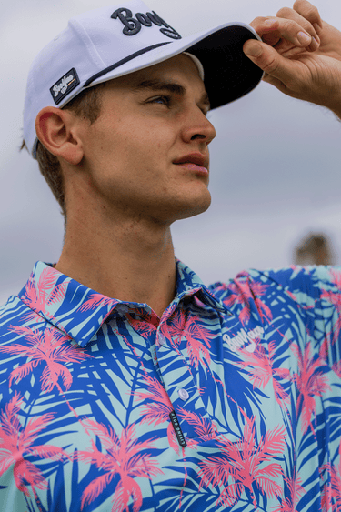 MAUI - PREMIUM LIFESTYLE COLLECTION 2026 - BOOYAA GOLF SHIRT, blue and pink, three-quarter portrait with hand on cap